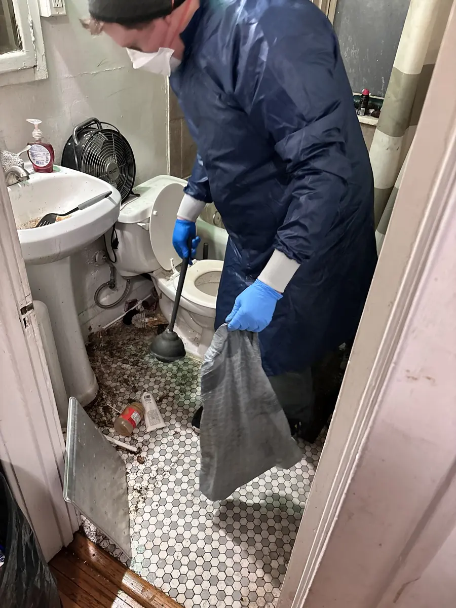 Crew member clearing debris from a neglected bathroom floor