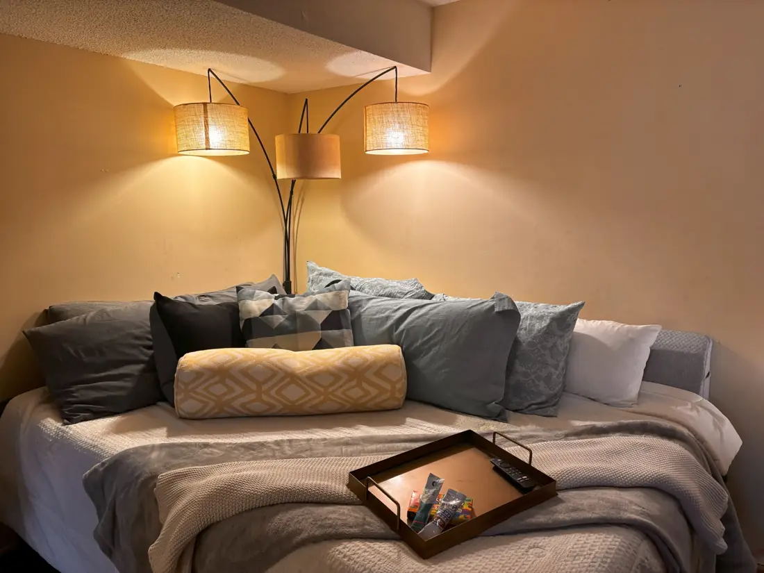Freshly made bed with layered pillows under a warm arc lamp